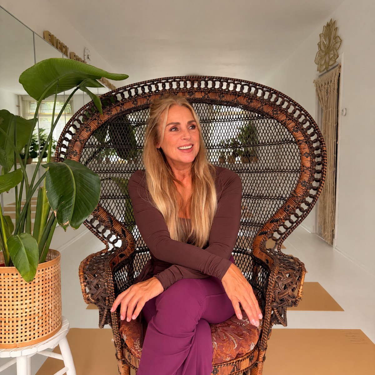 Karina Hermans zit lachend in een rotan stoel in haar yoga & pilates studio